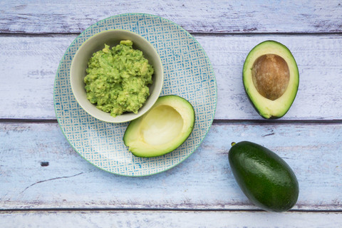 Schale mit Guacamole und ganzen und geschnittenen Avocados auf hellblauem Holz, lizenzfreies Stockfoto