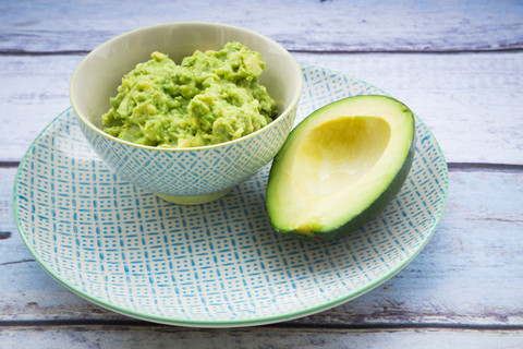 Bowl of Guacamole and half of an avocado on a plate stock photo