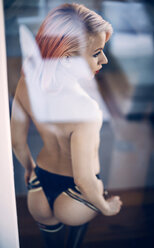 Erotische blonde Frau mit nackter Brust hinter Glasscheibe stehend - EHF000312
