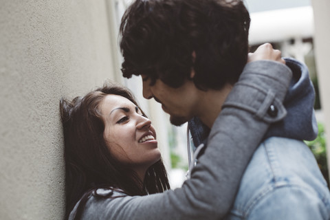 Junges Paar an Hauswand beim Küssen, lizenzfreies Stockfoto