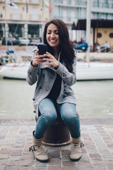 Italien, Rimini, junge Frau überprüft das Handy am Hafen - GIOF000448