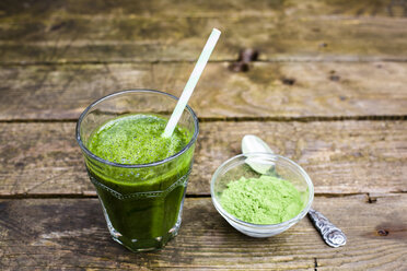 Glass of wheatgrass smoothie and bowl with wheatgrass powder on wood - SARF002291