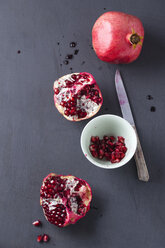 Whole and sliced pomegranate, kichen knife, and bowl of pomegranate seeds - MYF001198