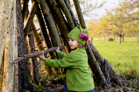 Little girl building a hut with logs on a meadow in autumn stock photo