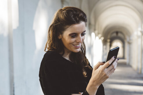 Lächelnde Frau, die in einer Spielhalle auf ihr Mobiltelefon schaut - GIOF000467