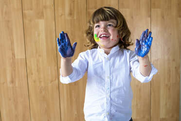 Porträt eines lächelnden kleinen Jungen, der seine Handflächen voller blauer Fingerfarbe zeigt - KIJF000007