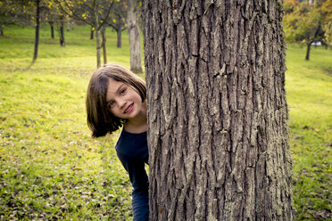 Porträt eines Mädchens, das sich hinter einem Baumstamm versteckt - LVF004144