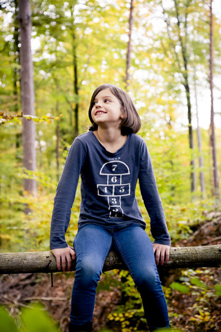 Porträt eines glücklichen Mädchens, das auf einem Pfahl im Wald sitzt, lizenzfreies Stockfoto