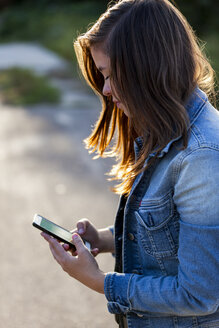 Teenager-Mädchen schaut auf Smartphone - HCF000154