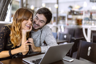 Happy young couple with laptop in a pub - MGOF001003