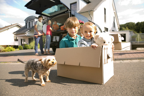 Zwei Brüder mit Hund im Karton auf der Straße mit Familie im Hintergrund, lizenzfreies Stockfoto