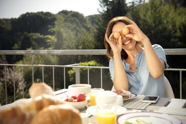 Verspielte Frau beim Frühstück auf dem Balkon - TOYF001428