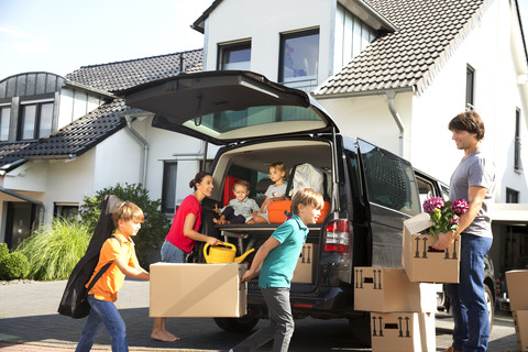 Happy family at driveway carrying cardboard boxes stock photo