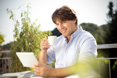 Smiling man with digital tablet and cup of coffee on balcony stock photo