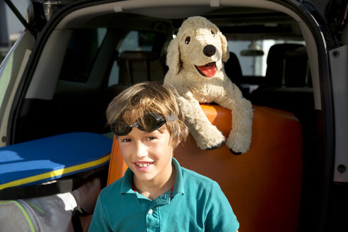 Lächelnder Junge im Kofferraum mit Schwimmbrille und Kuscheltier - TOYF001458