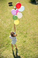 Woman standing in garden holding colorful balloons - TOYF001468