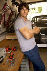 Smiling man in garage with bottle of beer and vintage car - TOYF001470