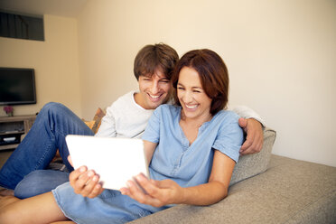 Happy couple relaxing on couch looking at digital tablet - TOYF001480