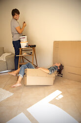 Laughing woman in cardboard box with man painting wall - TOYF001488