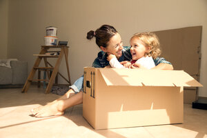 Laughing woman with daughter sitting in cardboard box - TOYF001492