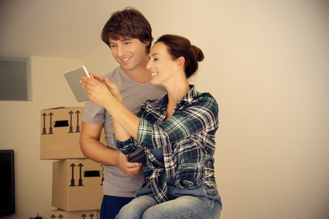 Smiling couple looking at digital tablet with cardboard boxes in background stock photo