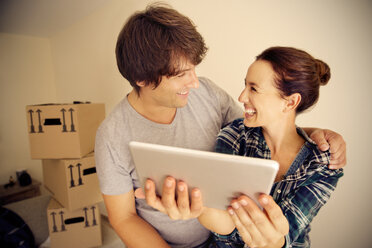 Glückliches Paar mit digitalem Tablet und Kartons im Hintergrund - TOYF001505