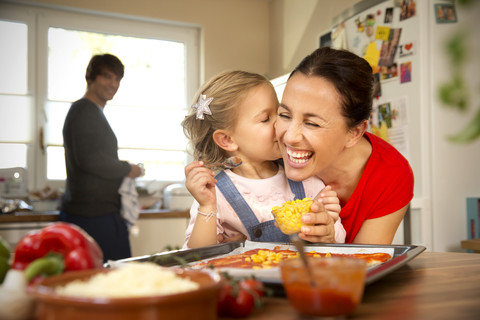 Happy mother and daughter in kitchen preparing pizza with father in background stock photo