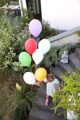 Mädchen läuft auf einer Treppe und hält bunte Luftballons - TOYF001524