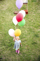 Girl standing in garden holding colorful balloons - TOYF001525
