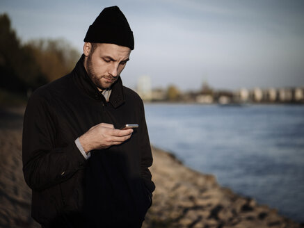 Deutschland, Köln, Mann steht mit seinem Smartphone am Rhein - DASF000021