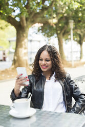 Portrait of smiling young woman sitting in a street cafe looking at her smartphone - RAEF000625