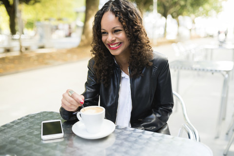 Porträt einer glücklichen jungen Frau mit einer Tasse Kaffee in einem Straßencafé, lizenzfreies Stockfoto