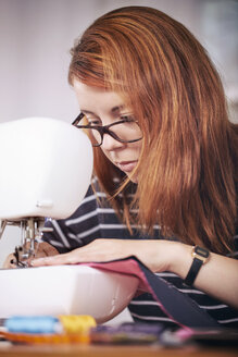 Portrait of young woman using sewing machine at home - SEGF000421