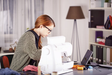 Portrait of young woman using sewing machine at home - SEGF000424