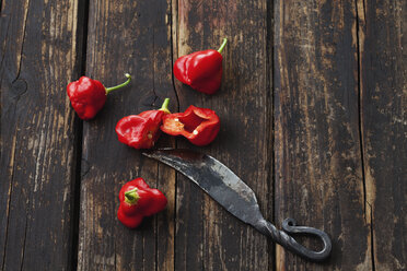 Whole and sliced red chili bell peppers and a knife on dark wood - CSF026701