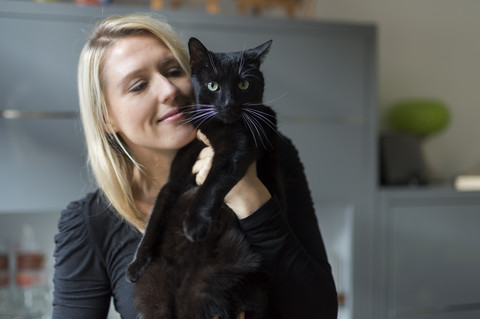 Porträt einer lächelnden blonden Frau, die ihre schwarze Katze hält, lizenzfreies Stockfoto