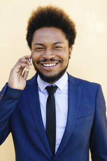 Porträt eines lächelnden jungen Geschäftsmannes, der mit einem Smartphone telefoniert - EBSF001009