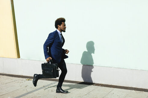 Junger Geschäftsmann mit Aktentasche läuft auf dem Bürgersteig - EBSF001012