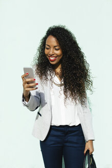 Porträt einer lächelnden jungen Geschäftsfrau, die auf ihr Smartphone schaut - EBSF001016