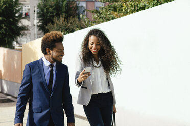 Portrait of two smiling young business people looking at smartphone - EBSF001017