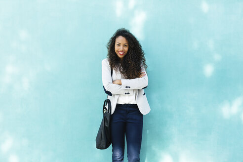 Porträt einer lächelnden jungen Geschäftsfrau mit Ledertasche, die vor einer blauen Wand steht - EBSF001020