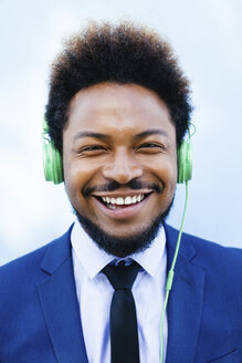 Porträt eines lächelnden jungen Geschäftsmannes, der mit Kopfhörern Musik hört - EBSF001021
