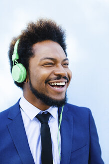 Porträt eines lächelnden jungen Geschäftsmannes, der mit Kopfhörern Musik hört - EBSF001022