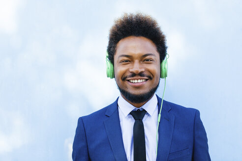 Porträt eines lächelnden jungen Geschäftsmannes, der mit Kopfhörern Musik hört - EBSF001023