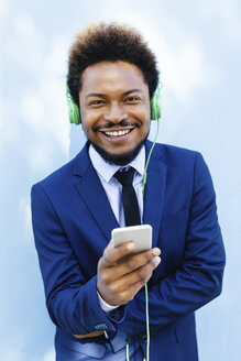 Porträt eines lächelnden jungen Geschäftsmannes, der mit Kopfhörern Musik hört - EBSF001024