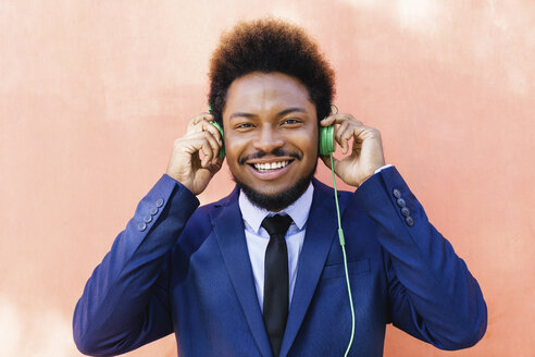 Porträt eines lächelnden jungen Geschäftsmannes, der mit Kopfhörern Musik hört - EBSF001025