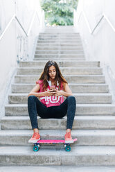 Porträt eines jungen Mädchens, das mit seinem Skateboard auf einer Treppe sitzt und sein Smartphone benutzt - GEMF000468