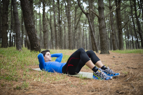 Sportler übt Sit-ups im Wald, lizenzfreies Stockfoto
