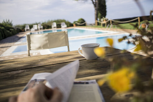 Italien, Toskana, Person liest Buch, sitzt am Tisch am Pool - RIBF000387