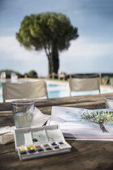 Italien, Toskana, Aquarelle, Papier und Malerei auf einem Tisch am Pool - RIBF000388